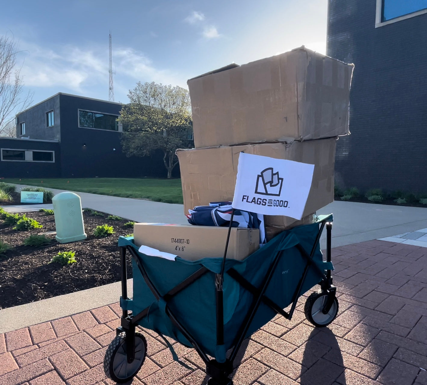 A foldable cart named Disco Jeff filled with boxes and a Flags For Good logo flag on the corner.