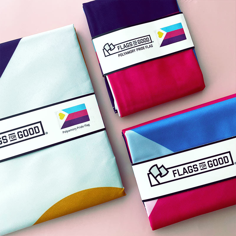 Polyamorous Pride Flags in various sizes folded in Flags For Good Packaging sitting on a pink table.