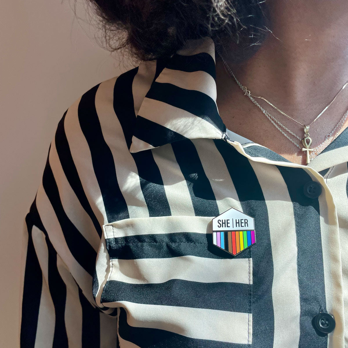 Woman wearing a Flags For Good Pronoun + Pride Flag Magenetic Pin with She Her pronouns and a rainbow flag