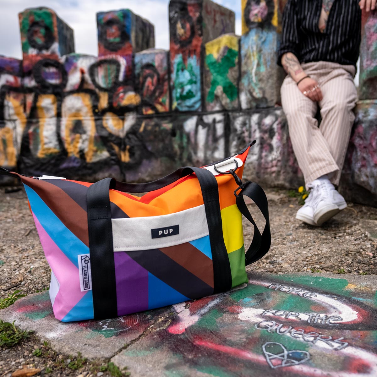 Upcycled Progress Pride Flag Weekender Bag in front of graffiti - Flags For Good X PUP