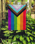 Progress Pride vertical Garden Flag designed by Daniel Quasar produced by Flags For Good in a garden
