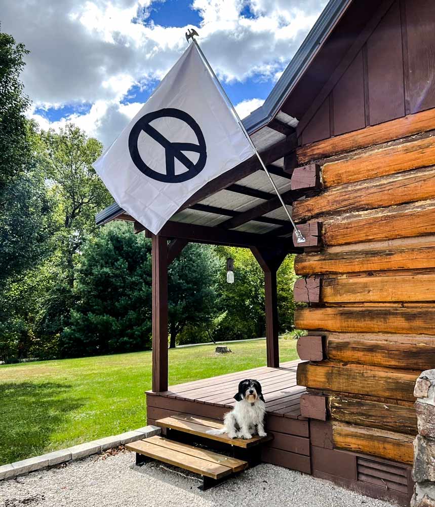 White peace sign flag on a log cabin with a dog on the porch