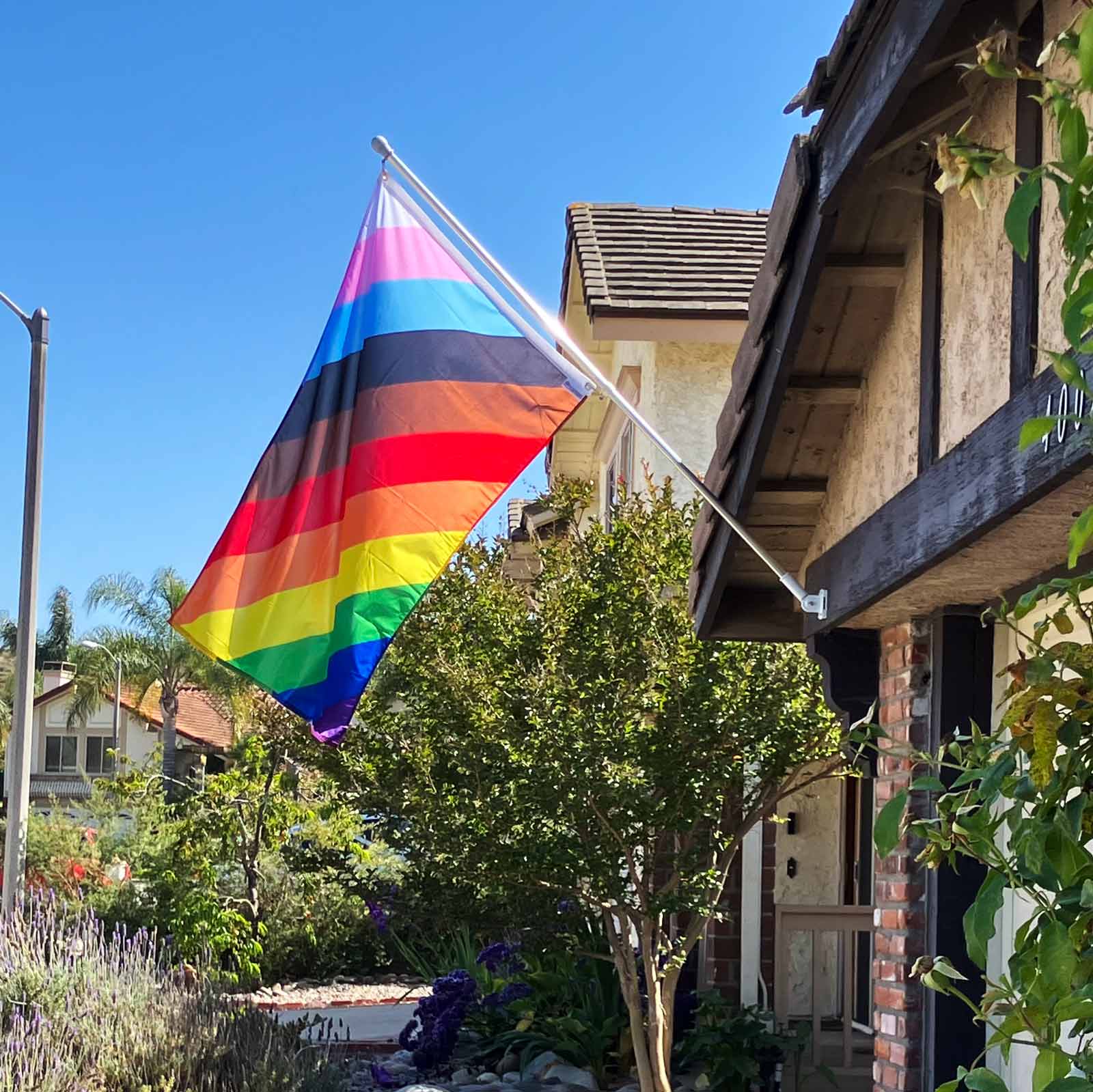 11-stripe diagonal LGBTQ Pride flag flying on a pole in front of a house