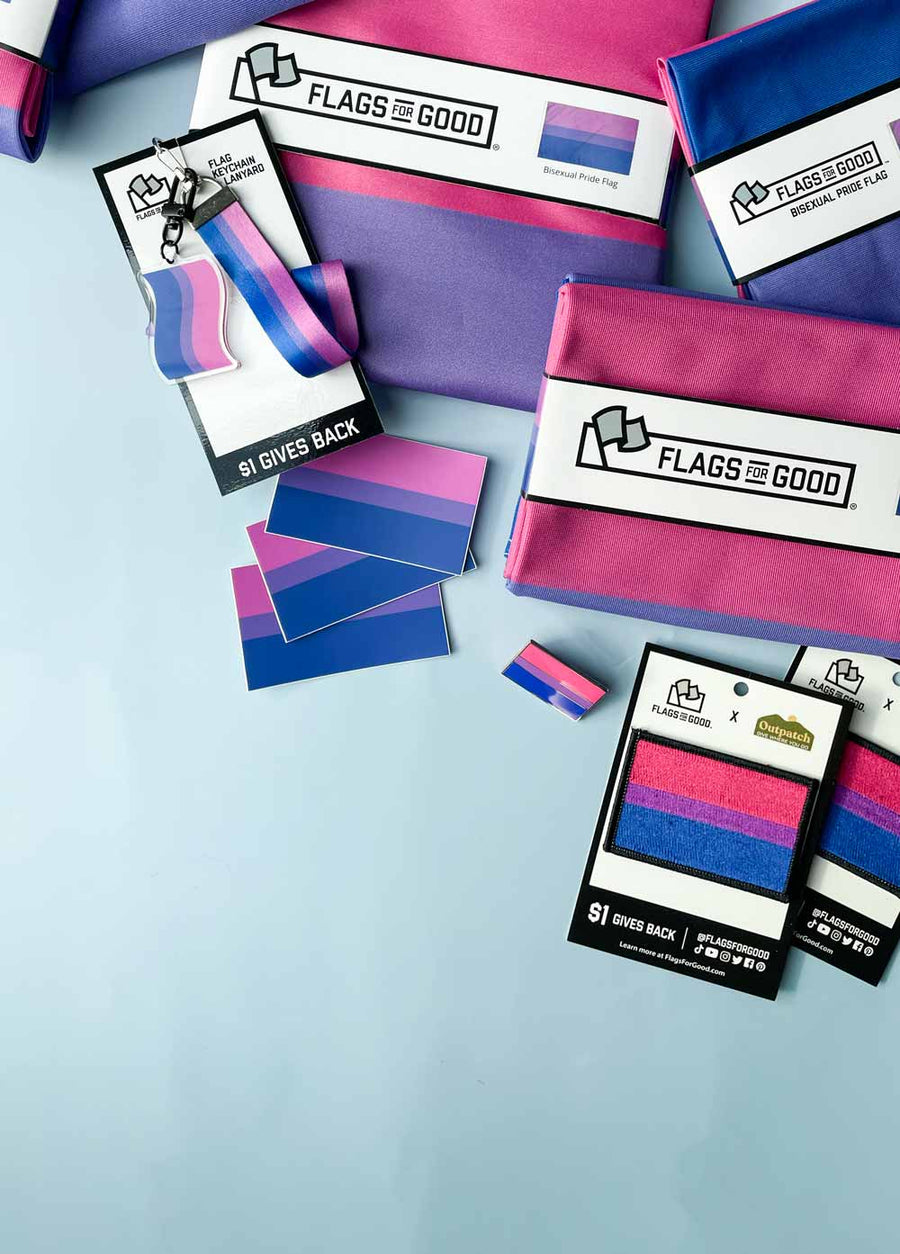 Bisexual Pride Flags, keychains, stickers and patches strewn around on a blue background