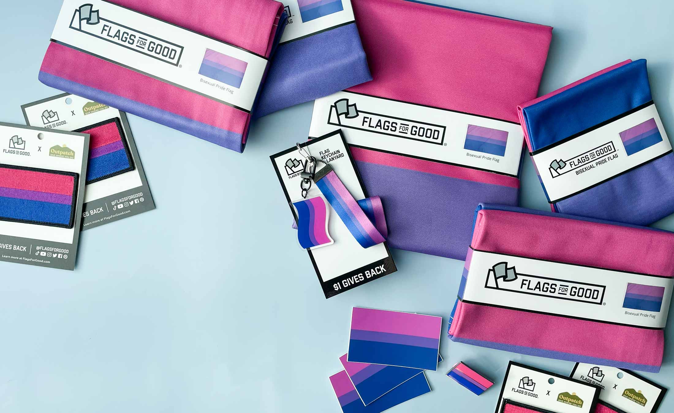 Bisexual Pride Flags, keychains, stickers and patches strewn around on a blue background