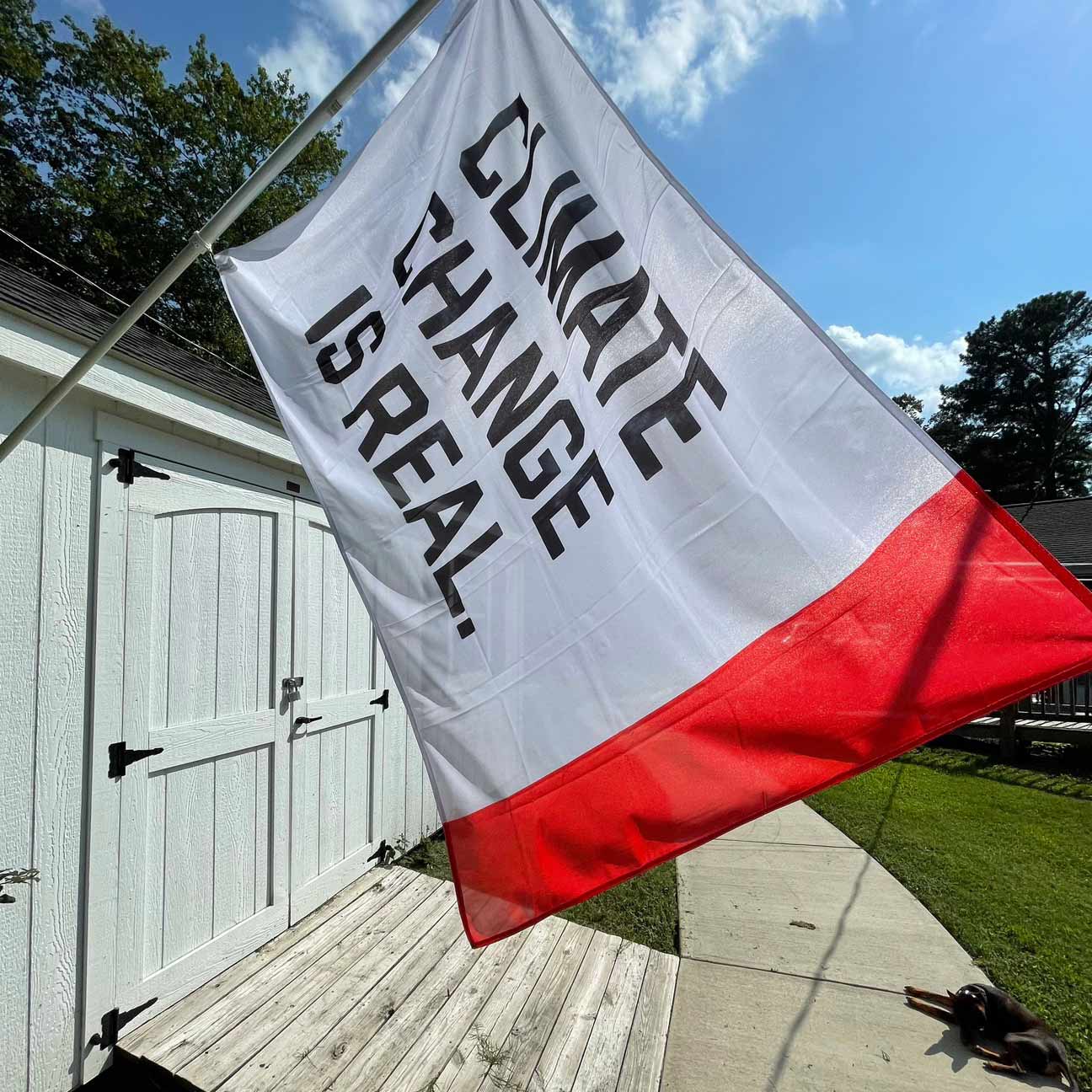 Climate Change Is Real Flag flying on a flag pole from a garage