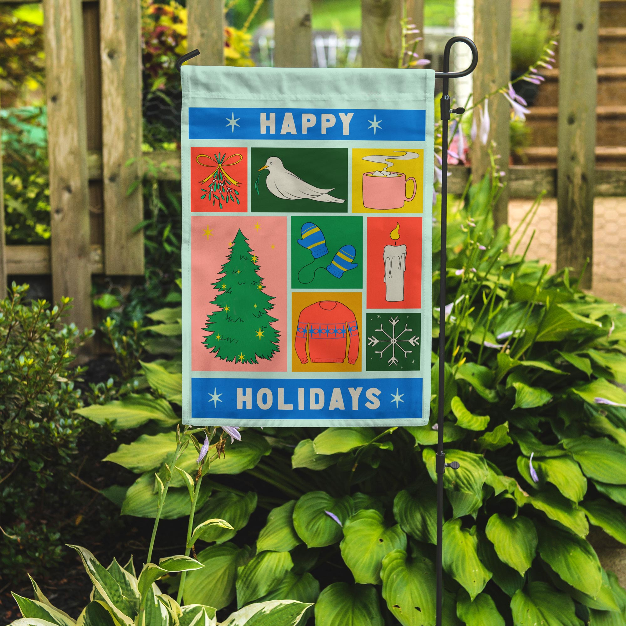 Decorative garden flag with holiday-themed design on a stand among green plants.