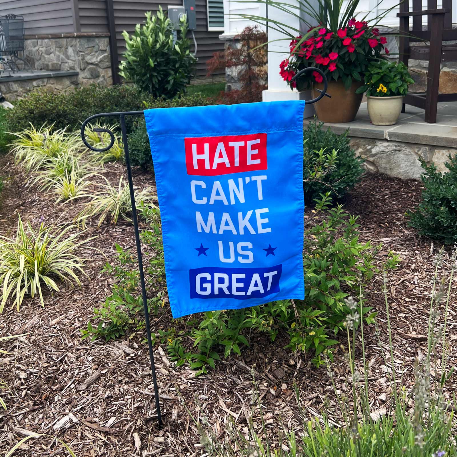 "Hate Can't Make Us Great" blue garden flag by Flags For Good in a garden