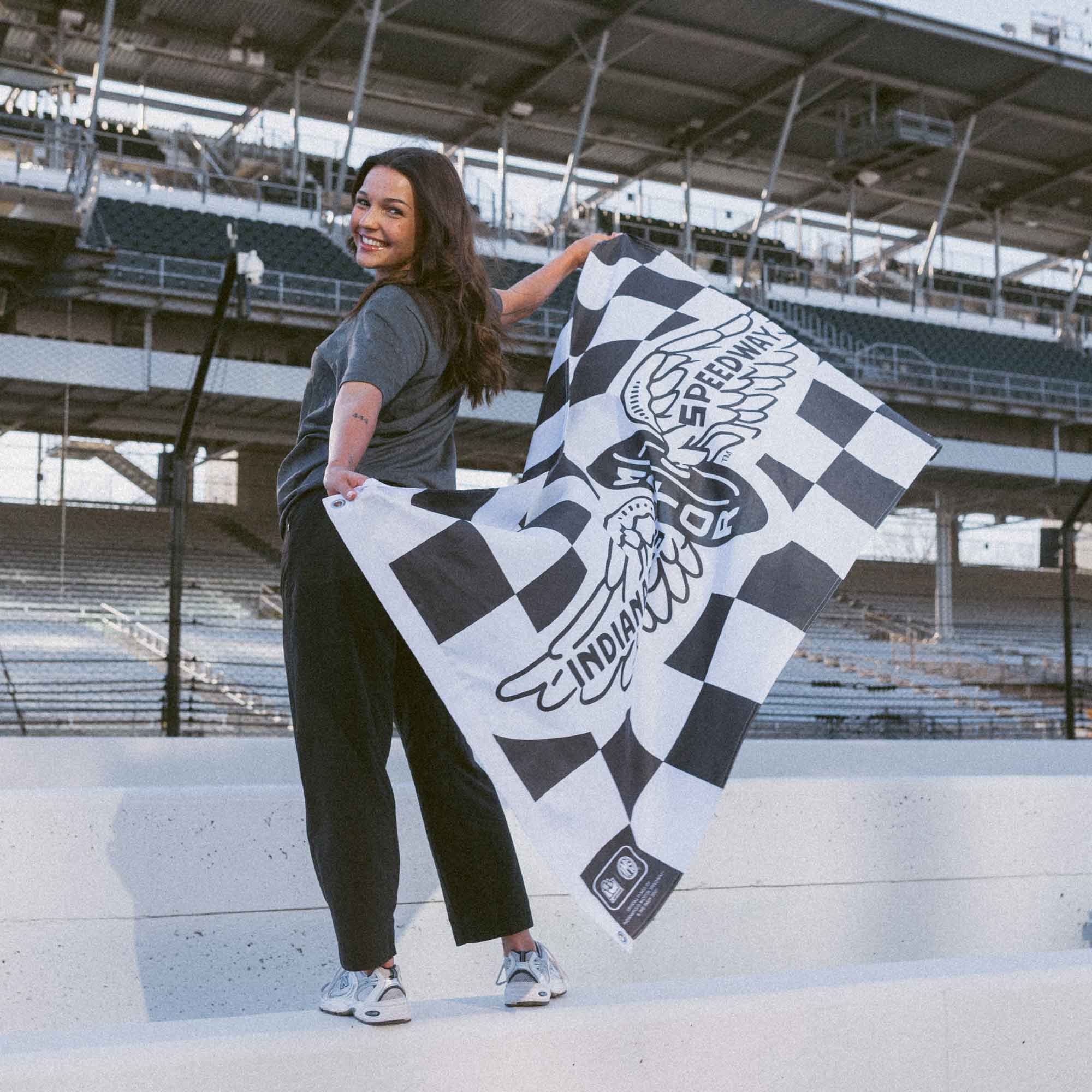 Woman holding a checkered flag with a vintage IMS logo at the track