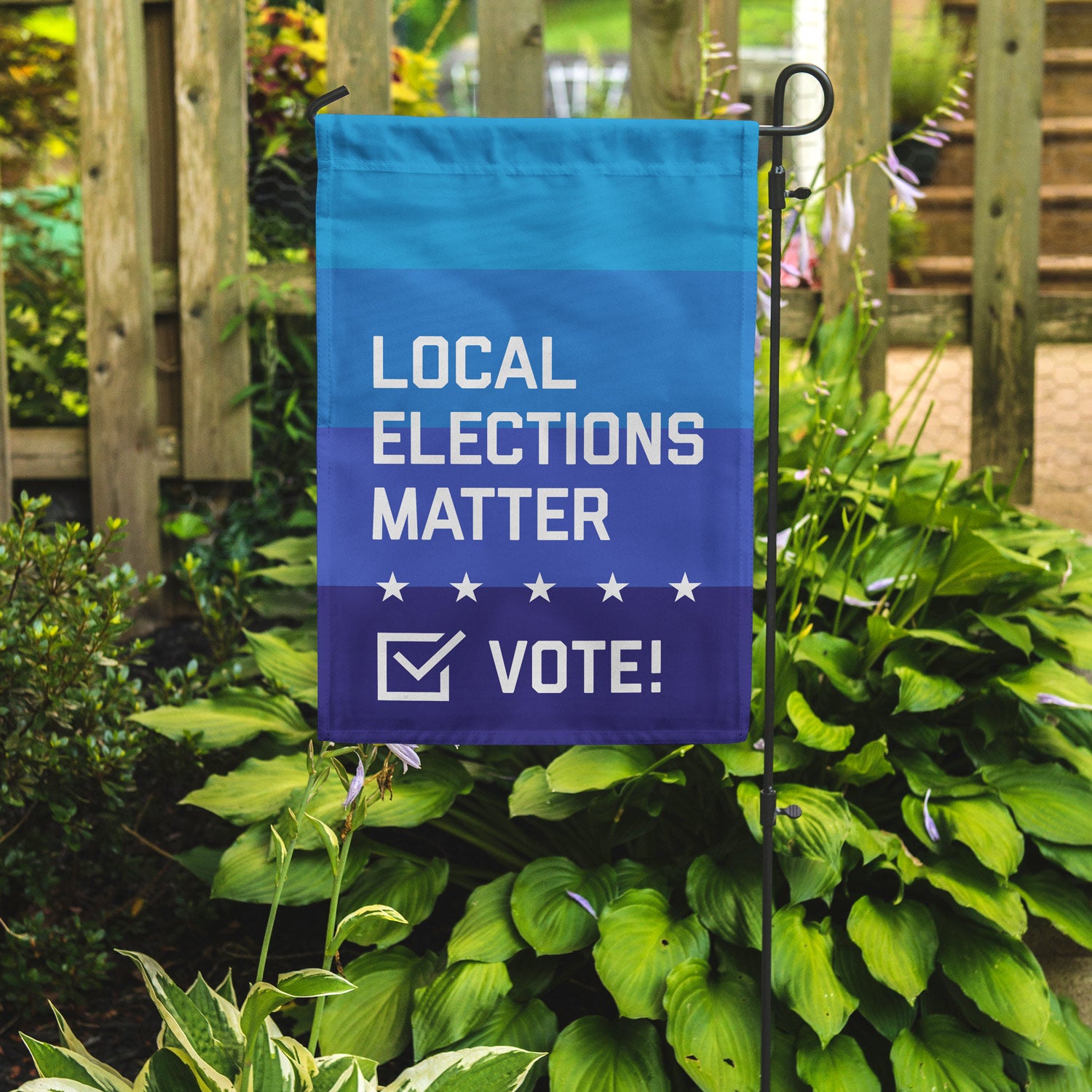 Local elections matter garden flag on a garden pole in front of some plants