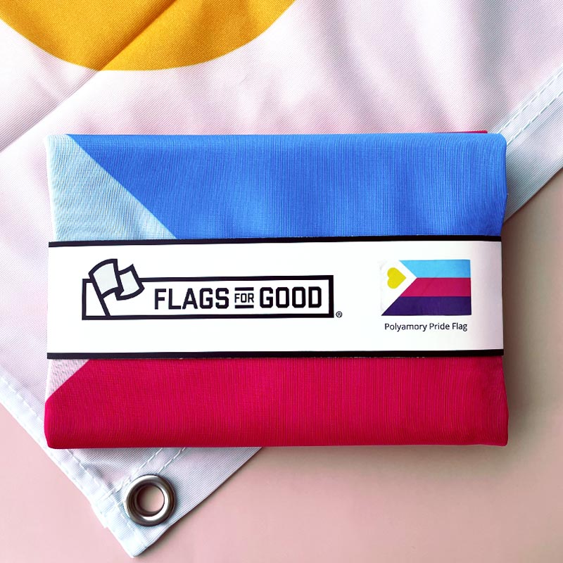 Polyamorous Pride Flag folded in Flags For Good packaging sitting on top of an unfolded flag showing the grommet.