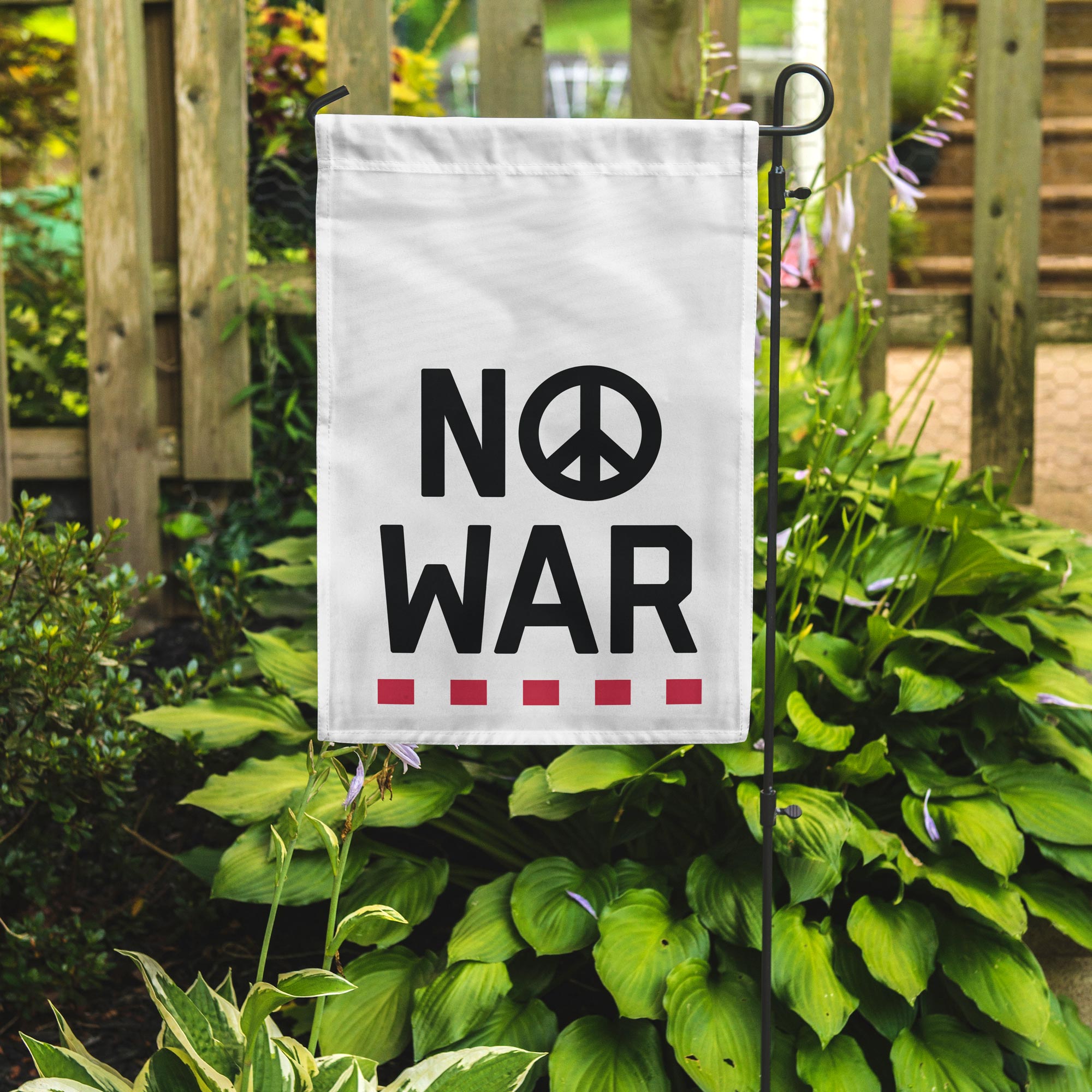 Garden flag with 'No War' text and peace symbol on a stand in a garden setting.
