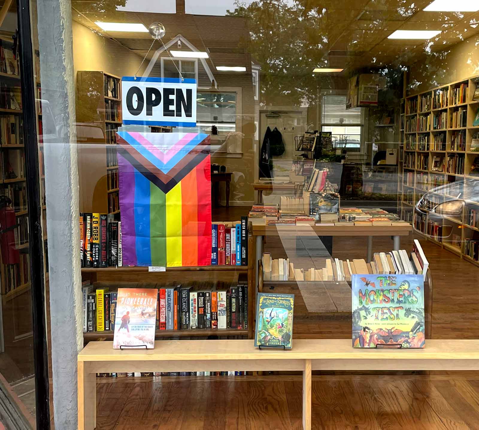 Progress Pride Garden Flag hanging in a window below an OPEN sign