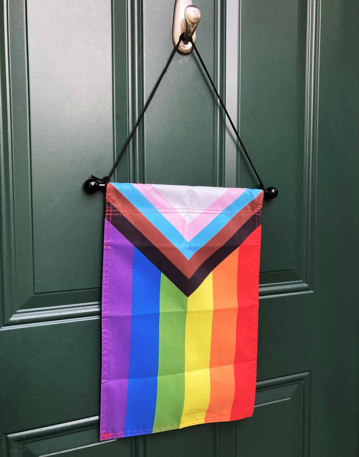 Progress Pride vertical Garden Flag by Flags For Good hanging on a door