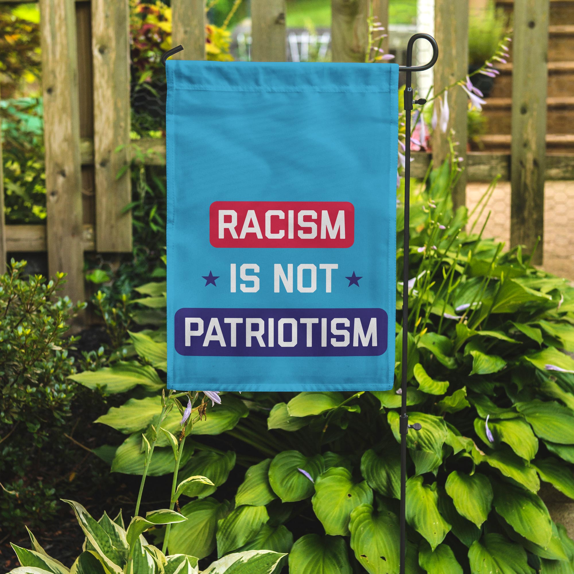 Garden flag with 'Racism is not patriotism' text in a garden setting
