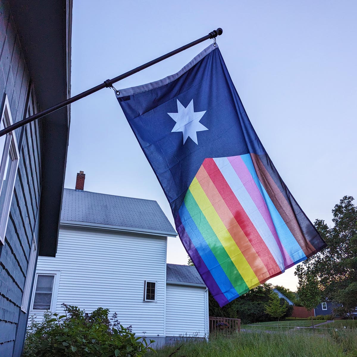 New 2023 Minnesota State Flag with Rainbow Stripes in the fly edge on a flag pole off of a house