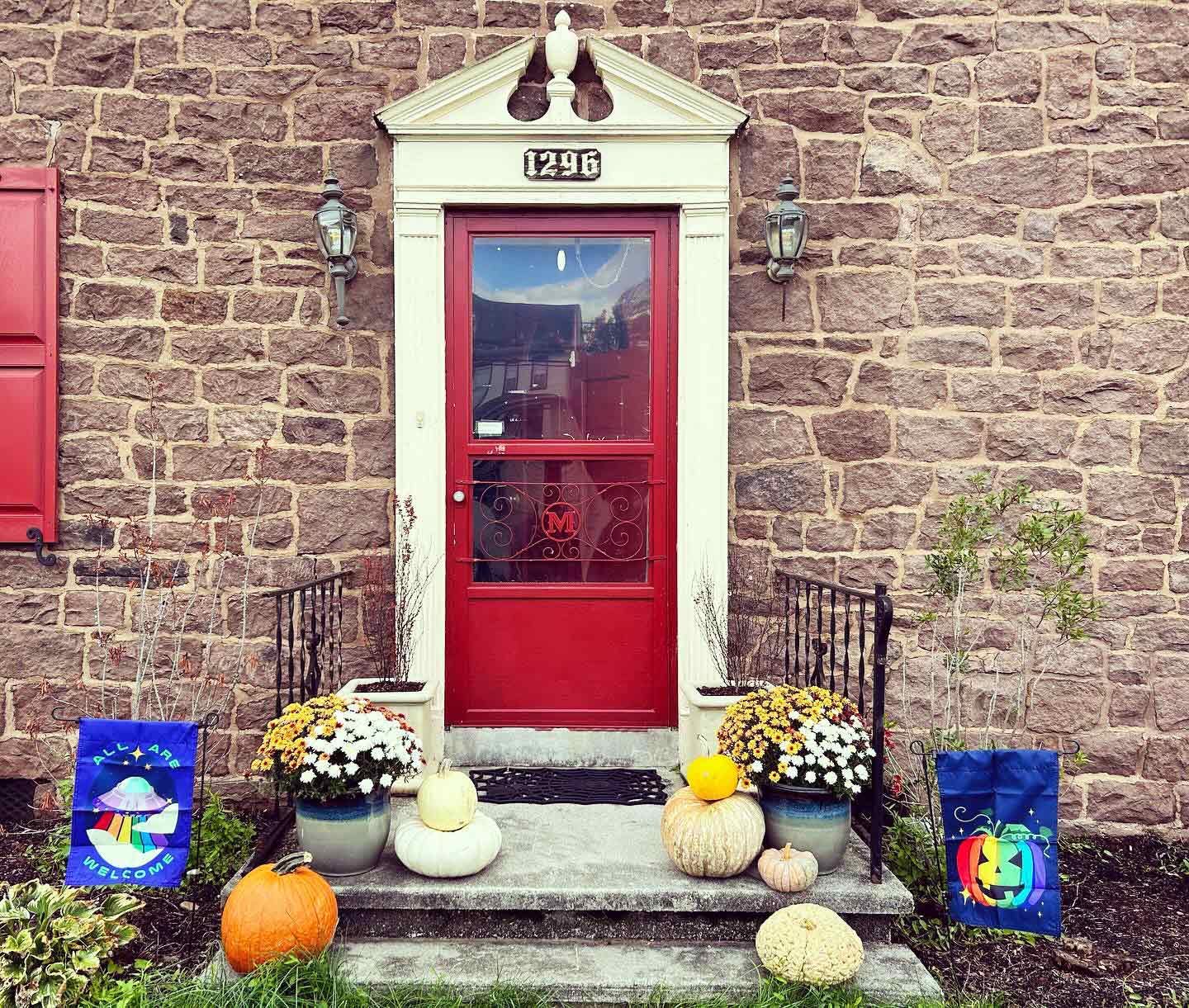 rainbow pumpkin garden flag next to a red door surrounded by pumpkins