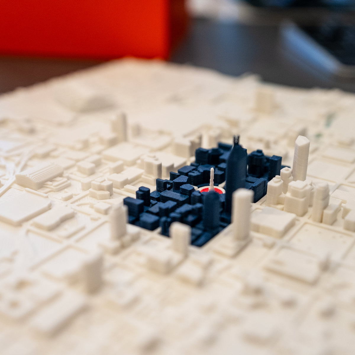 A close-up of Monument Circle in a miniature Indianapolis city map 3D model, featuring dark blue blocks and a red circle showing how the city flag is born from the city grid. 