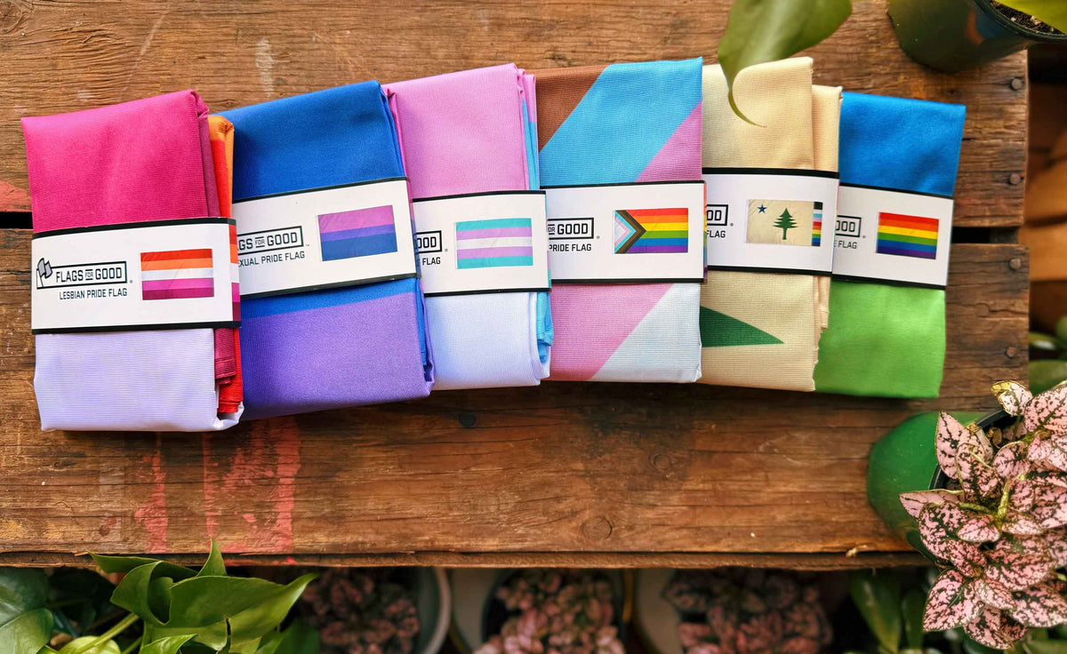 Colorful various lgbtq folded pride flags with Flags For Good brand labels on a wooden surface