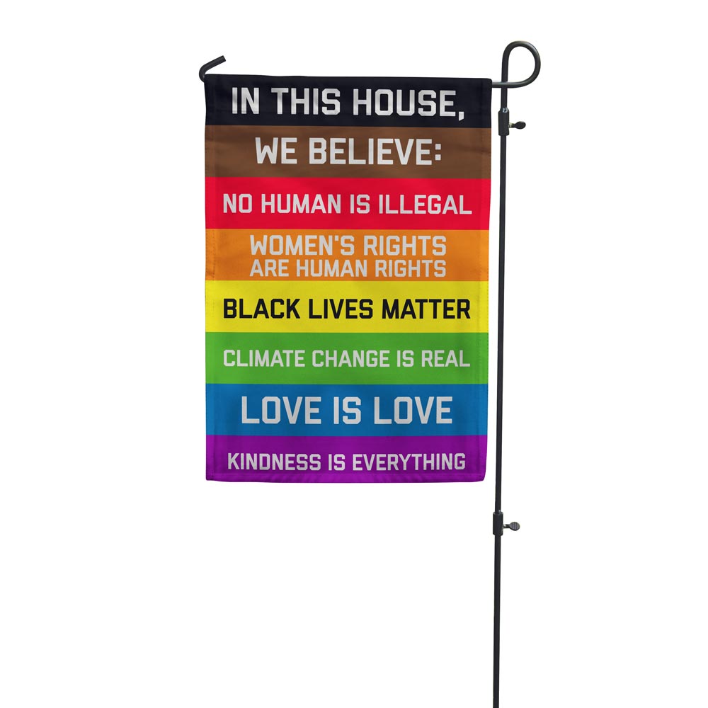 "In this House We Believe: No human is Illegal, Women's RIghts are Human Rights, Black Lives Matter, Cliamate Change is Real, Love is Love, Kindness is everything" garden flag hanging on a stand