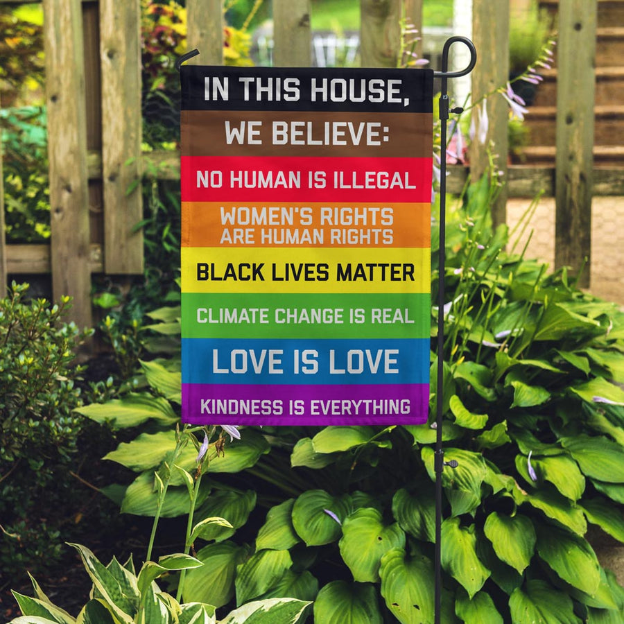 "In this House" garden flag placed in a garden
