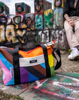 Upcycled Progress Pride Flag Weekender Bag in front of graffiti  - Flags For Good X PUP