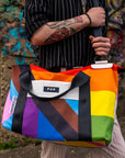Upcycled Progress Pride Flag Weekender Bag being held by someone in front of graffiti - Flags For Good X PUP