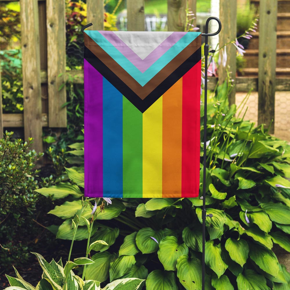 Progress Pride vertical Garden Flag designed by Daniel Quasar produced by Flags For Good in a garden