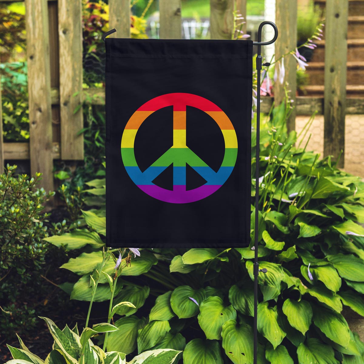 Rainbow Peace Sign on a black garden flag hanging on a pole in a garden
